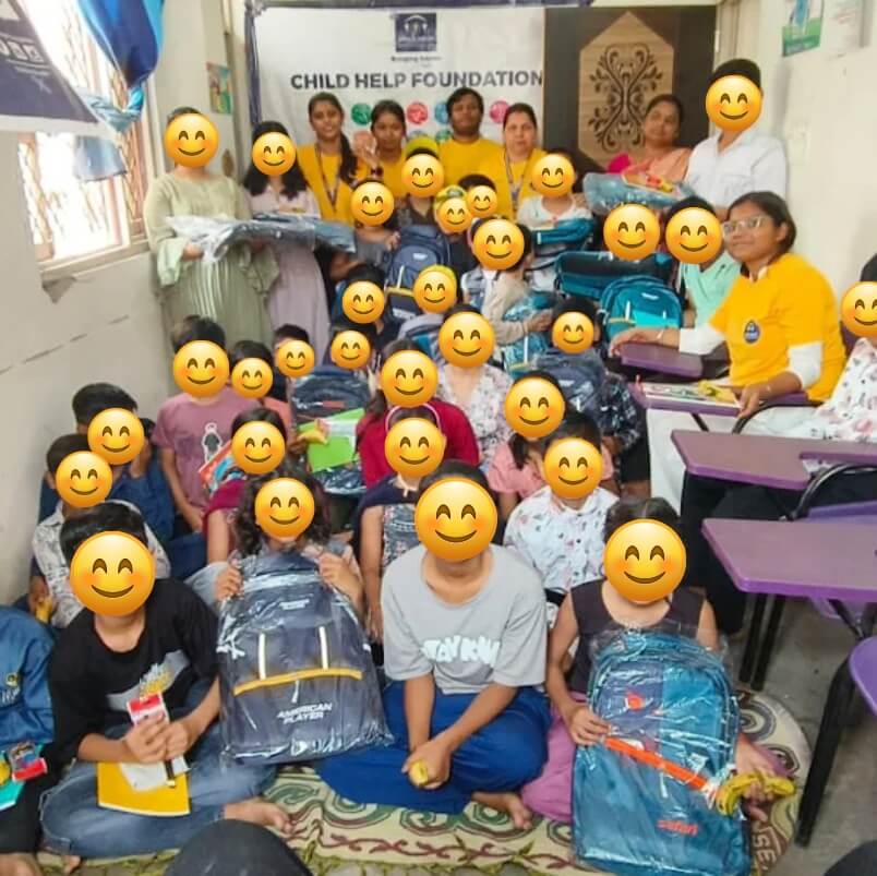 Child Help Foundation staff distribute school bags and educational supplies to underprivileged children in a classroom. Faces are covered with smiley emojis to protect identities.