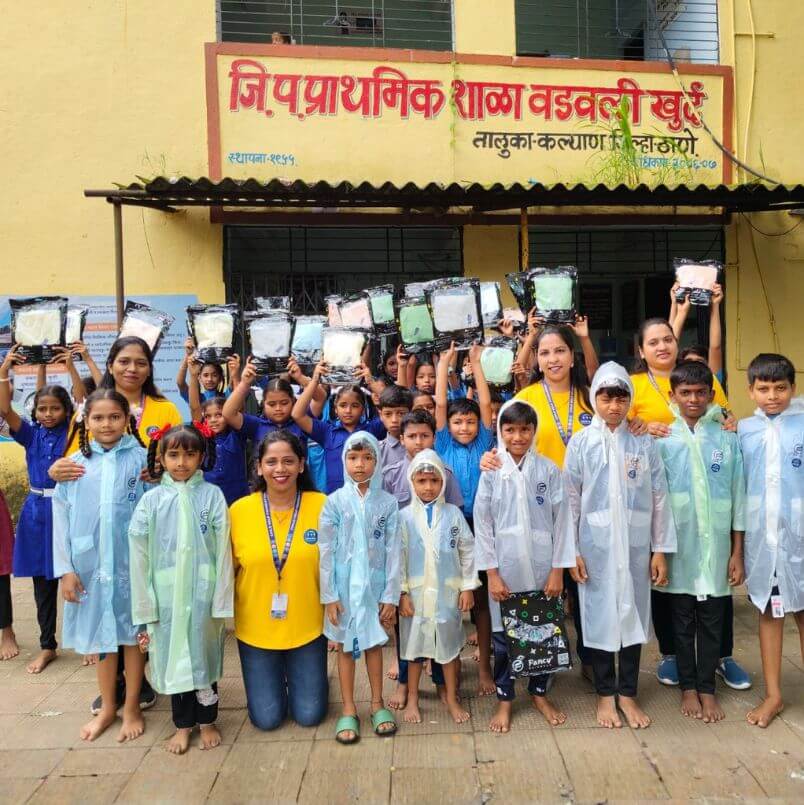 Child Help Foundation volunteers distributing raincoats and waterproof bags to children outside a primary school during monsoon season